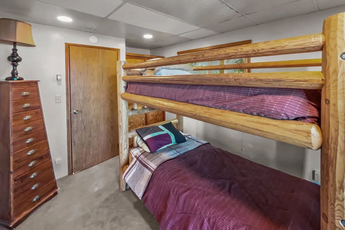 A bunkroom designed for comfort and fun, featuring a sturdy bunk bed, wooden dresser, and bedside lamp. The space is inviting for children or cousins to share stories and laughter before bed.