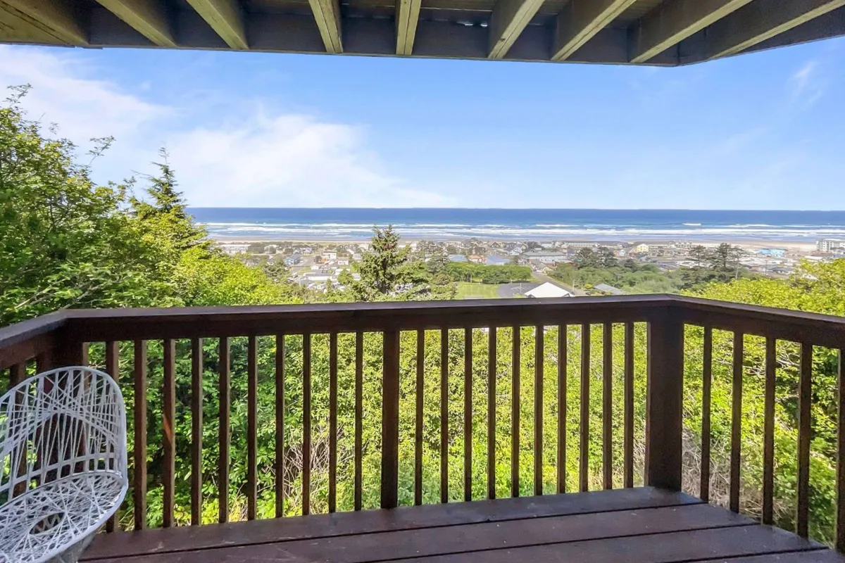 From this deck, the vantage point is framed by railing and lush surrounding greenery, with the ocean's expanse stretching beyond. The peaceful setting is ideal for quiet moments, reading, or wildlife watching as the sun rises.