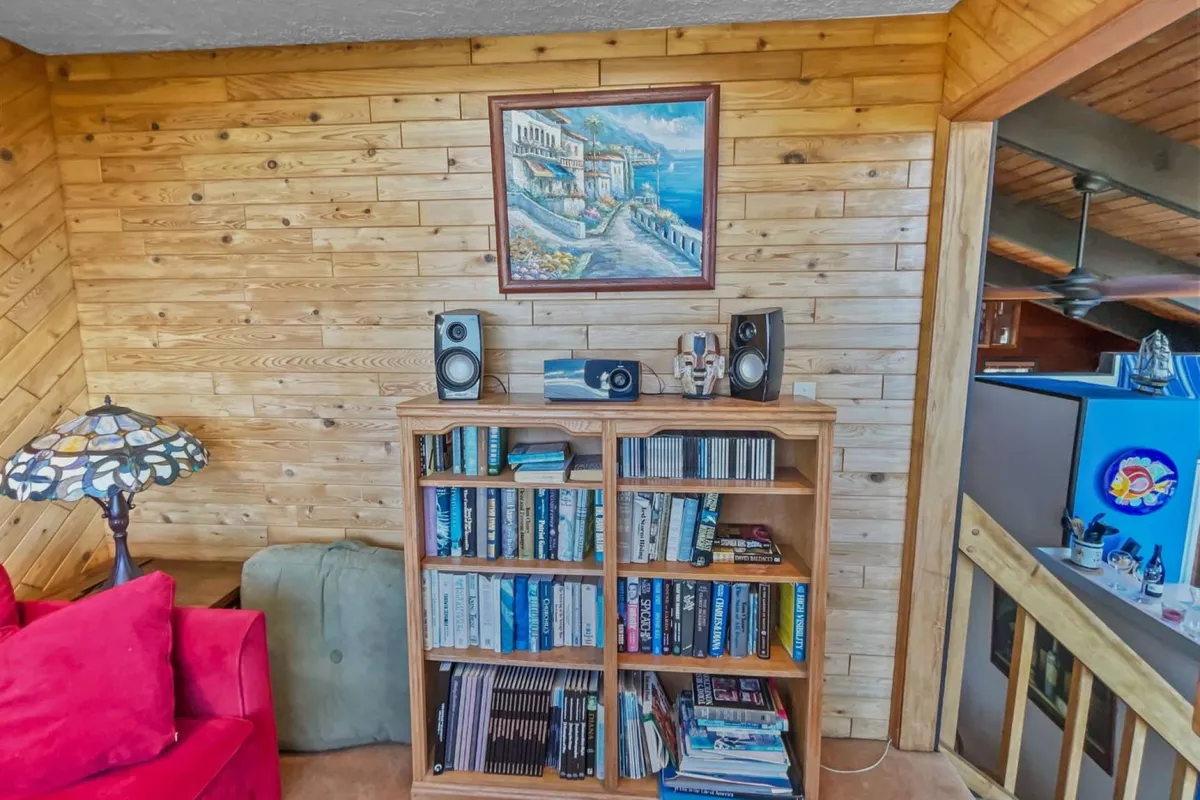 A cozy reading nook is shown, complete with a red couch, a bookshelf brimming with books, a colorful painting on the wall, and a unique lamp providing warm light. The scene evokes quiet moments of relaxation or focused work in an inviting atmosphere.