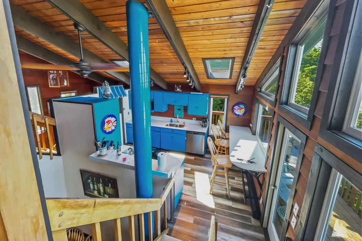This image features a bright, open-plan room with skylights, striking blue cabinetry, wooden beams, and vibrant wall art. The open staircase and natural light give the space an airy, uplifting feel, making it ideal for morning routines, casual work sessions, or unwinding after a day of exploration.