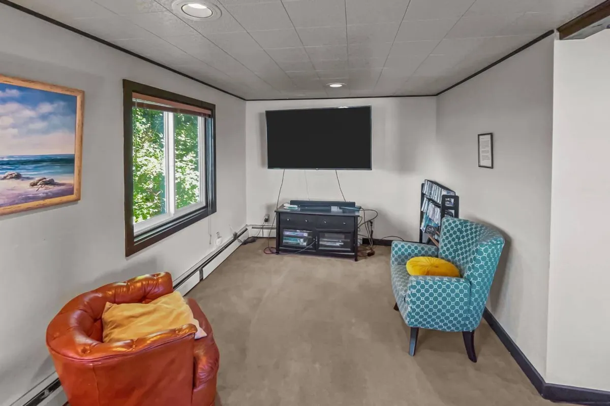 A spacious living area with a large window offering a scenic view, a wall-mounted TV, and colorful seating options arranged for relaxation or socializing. The room feels open and bright, with natural light streaming in from outside, suggesting an easy connection to the outdoors and a welcoming atmosphere for guests and their pets.
