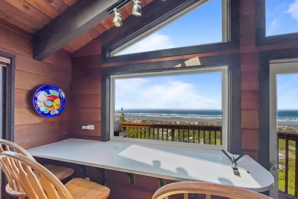 A loft-like space with large windows offering panoramic views, a stylish bar counter, and a colorful fish plate. The room feels airy and elevated, ideal for enjoying coffee, working remotely, or relaxing with friends.