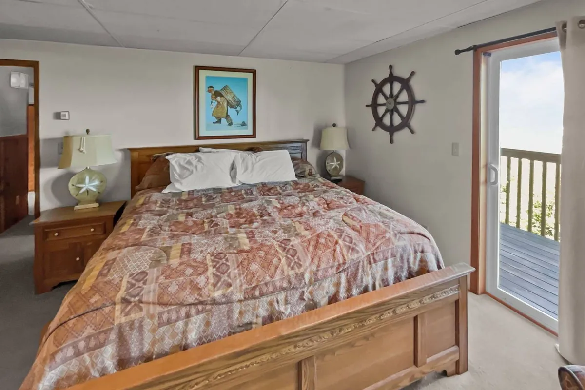 A serene bedroom setting featuring a bed with sunlight streaming in, complemented by artwork and lighthouse-themed decor. The space appears tranquil with hints of coastal influence, and it includes access to a balcony that hints at a connection to the outdoors.