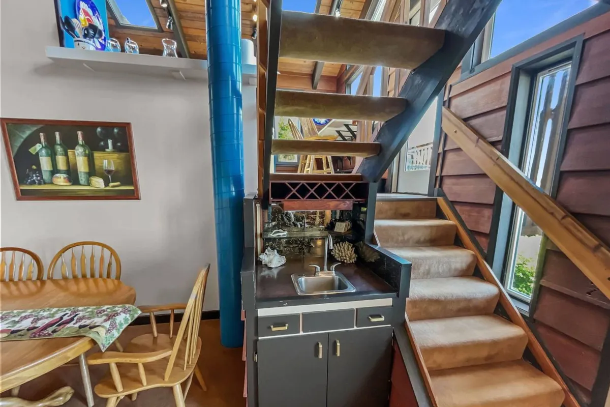 A spiral staircase stands beside a dining table, wine rack, and large windows that bathe the room in natural light. The space is designed for both dining and casual gatherings, with a warm, inviting atmosphere.