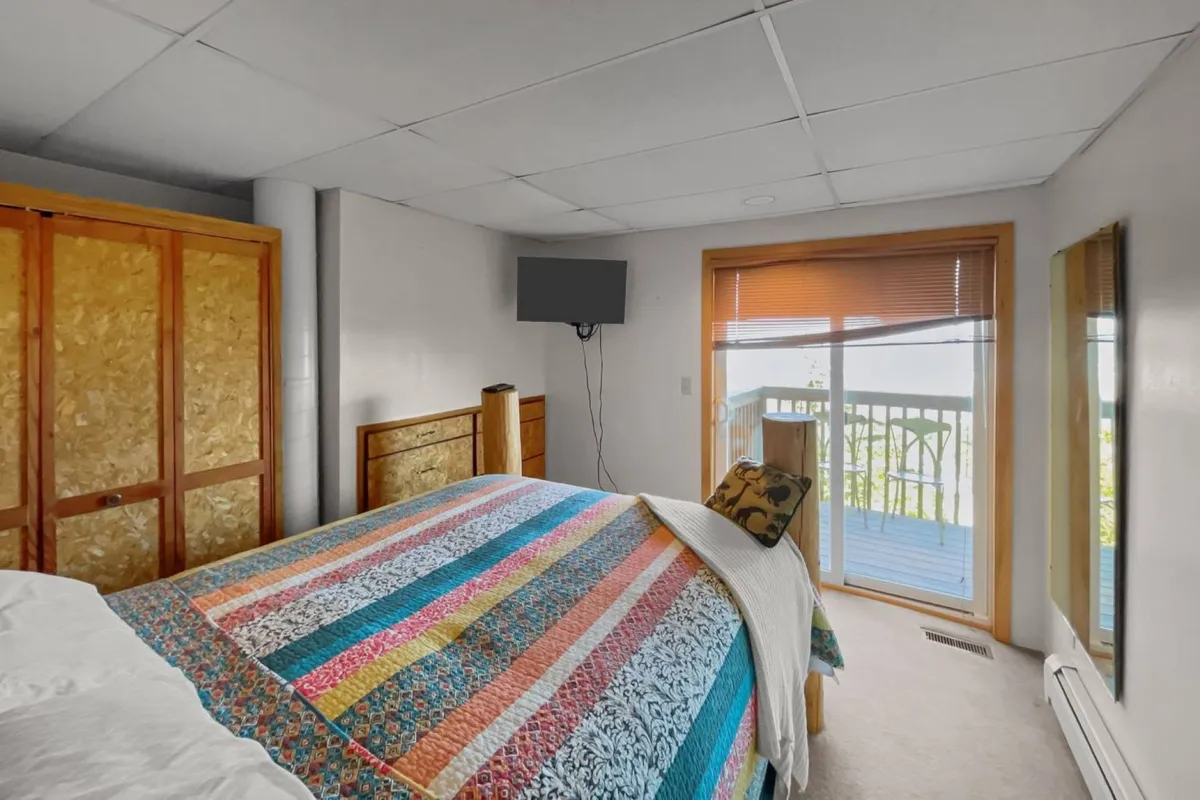 A cheerful bedroom with a colorful quilt, large window letting in natural light, a wooden closet, and a TV. The room feels comfortable and light-filled, perfect for relaxation.
