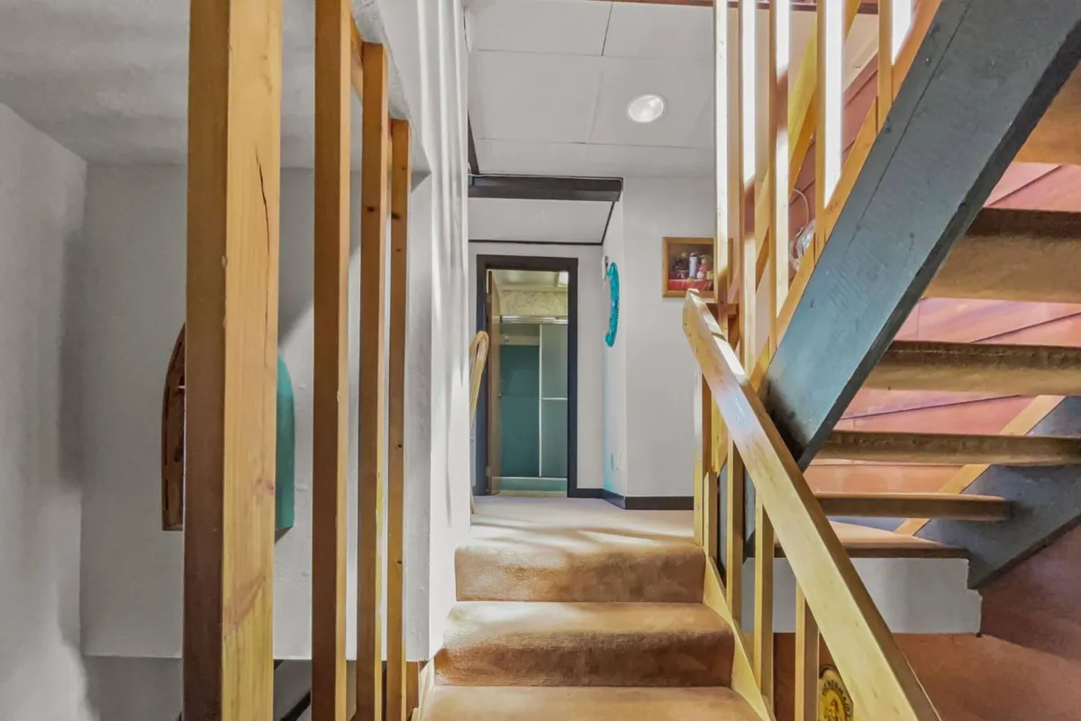 This image features a wooden railing and staircase, complemented by decorative items on the wall and a doorway leading to another space. The scene exudes a welcoming ambiance and a sense of connection between different areas of the home.
